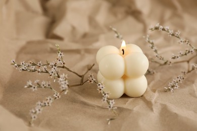 Photo of Burning soy candle and statice twigs on crumpled kraft paper