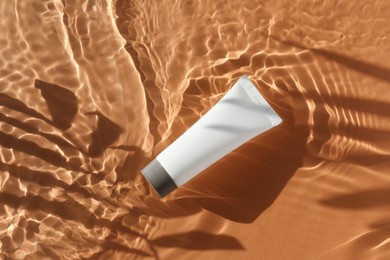 Tube with moisturizing cream in water and shadows from palm leaves on orange background, top view