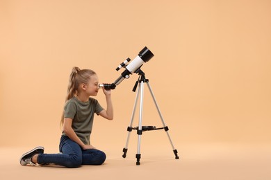 Little girl looking at stars through telescope on beige background, space for text