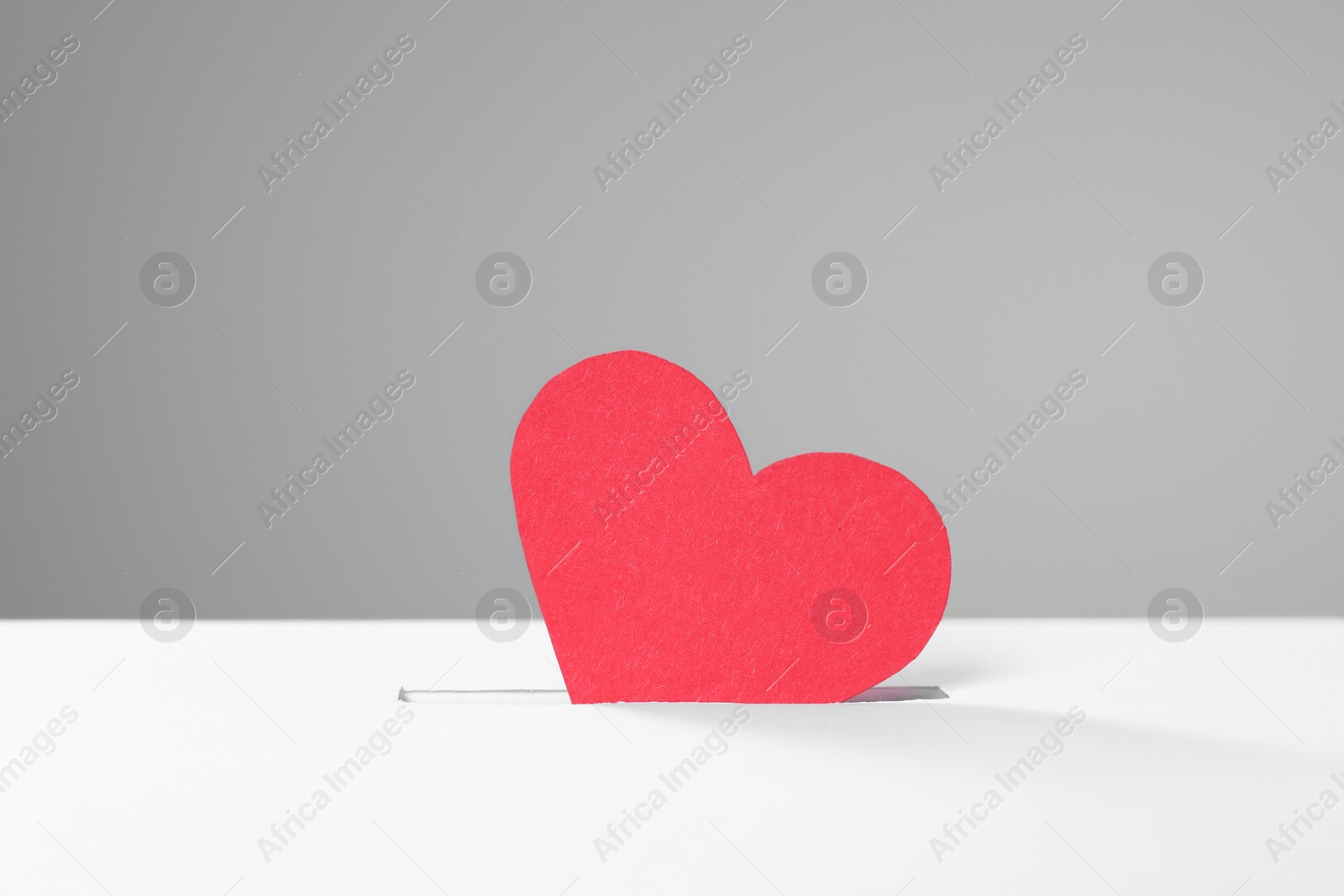 Photo of Red heart into slot of donation box against grey background