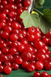 Many ripe red currants and leaves on green wooden table, closeup