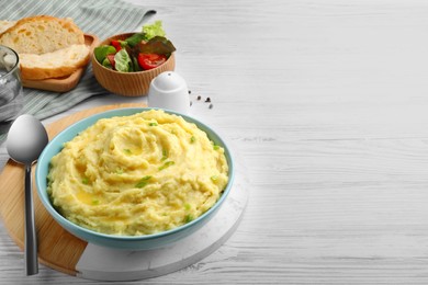 Bowl of tasty mashed potatoes with greens served on white wooden table. Space for text