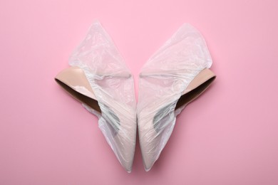 Photo of High heels in shoe covers on pink background, top view