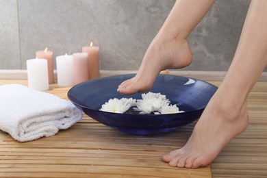 Photo of Woman soaking her feet in bowl with water and flowers on floor, closeup. Spa treatment