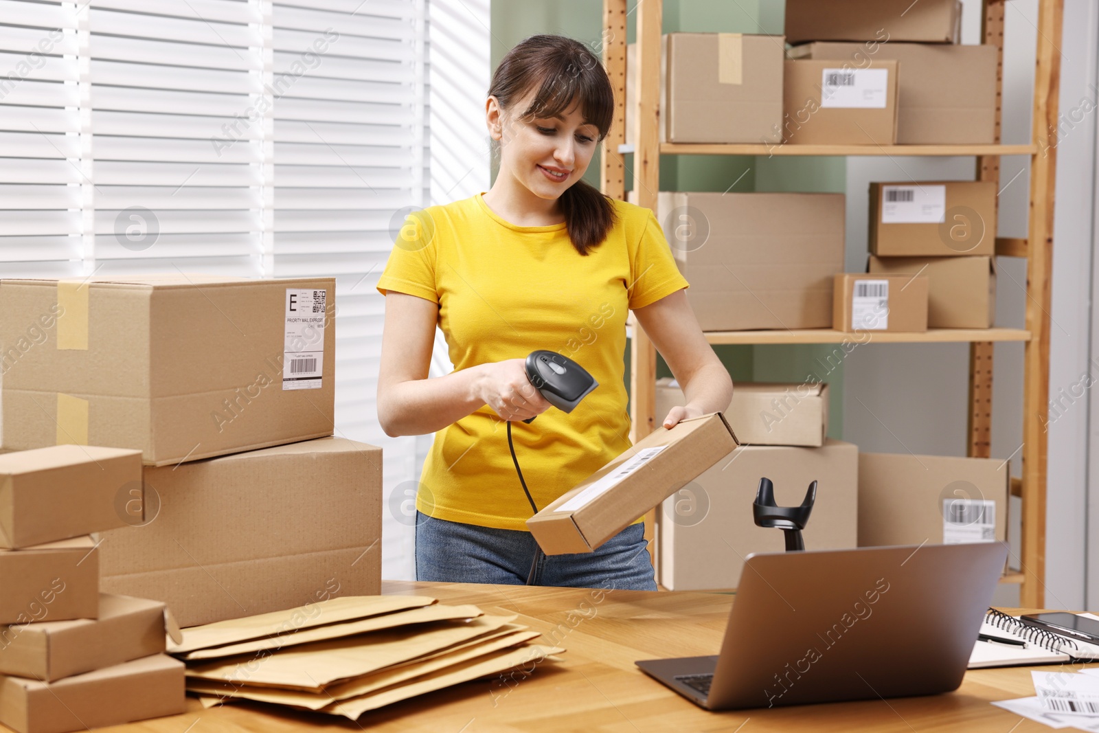 Photo of Parcel packing. Post office worker with scanner reading barcode at wooden table indoors