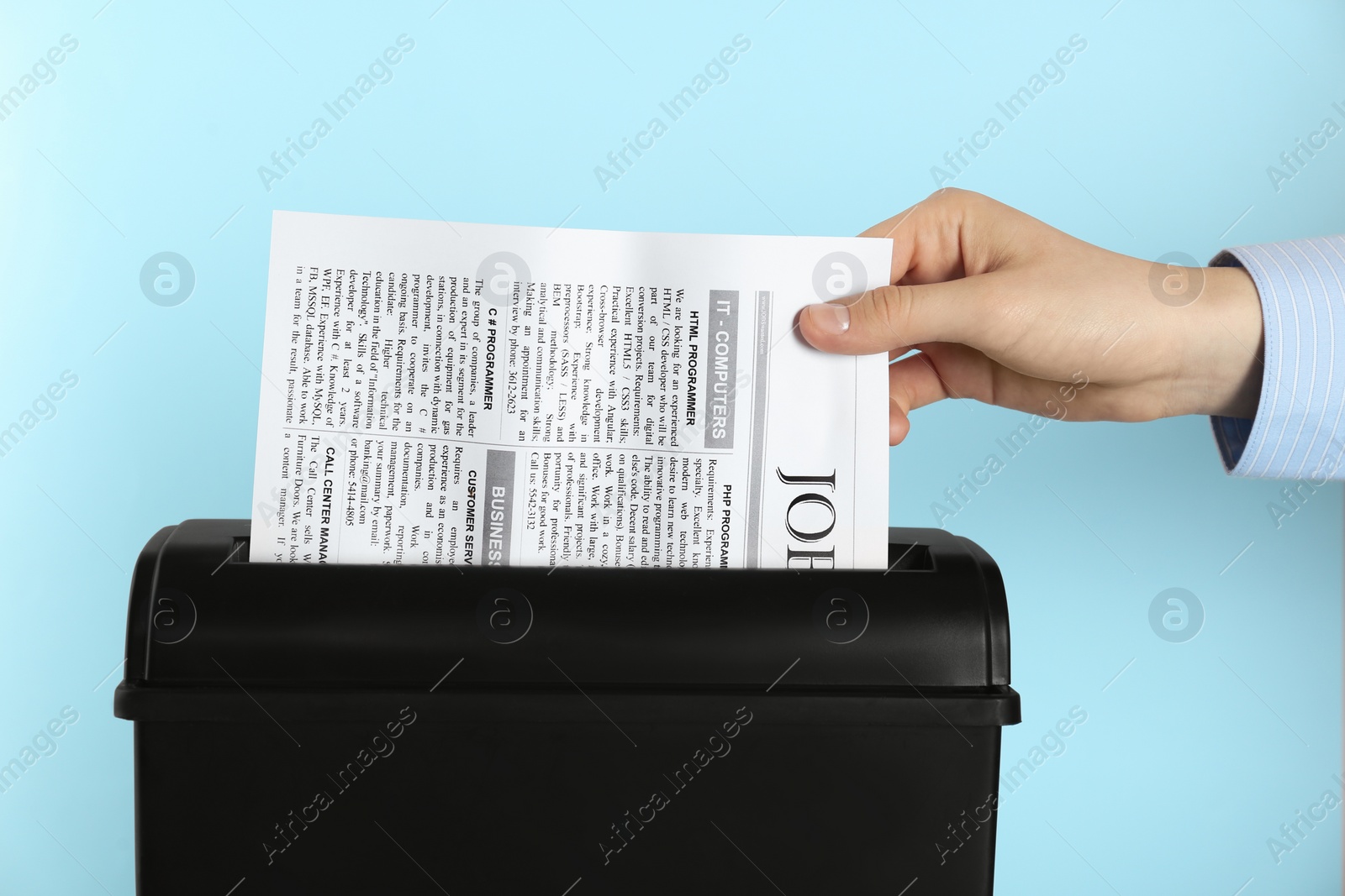 Photo of Woman destroying sheet of paper with shredder on light blue background, closeup