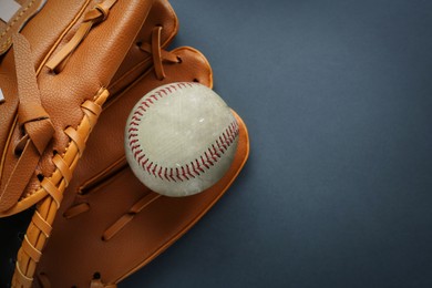 Catcher's mitt and worn baseball ball on dark background, top view. Space for text