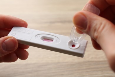 Woman dropping buffer solution onto disposable express test cassette at table, closeup