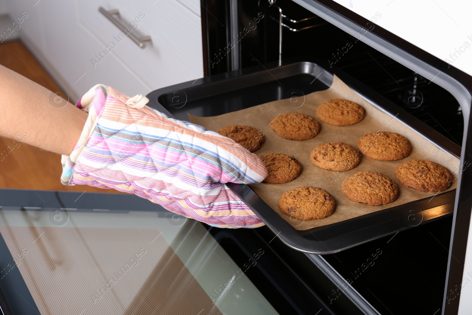 Photo of Woman taking baking tray with delicious cookies out of electric oven in kitchen, closeup