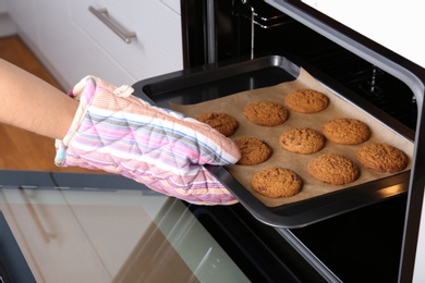 Photo of Woman taking baking tray with delicious cookies out of electric oven in kitchen, closeup