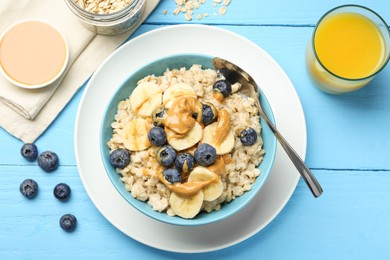 Tasty oatmeal with banana, blueberries and peanut butter served in bowl on light blue wooden table, flat lay