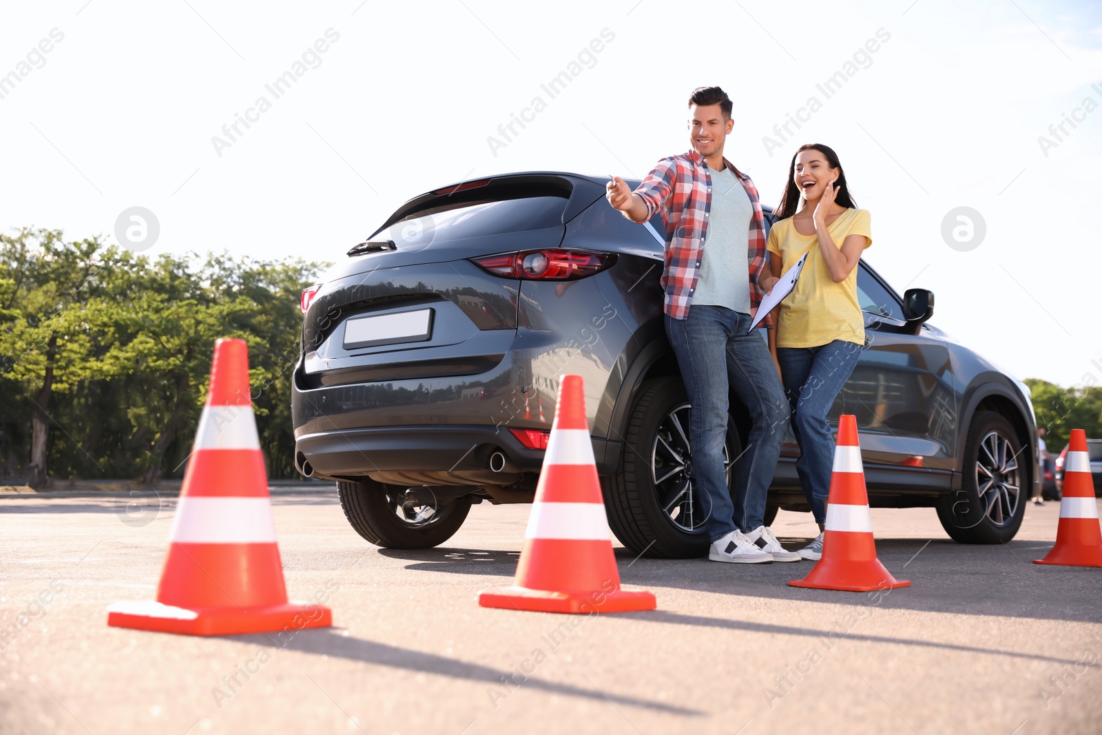 Photo of Instructor with clipboard and his student near car outdoors. Driving school exam