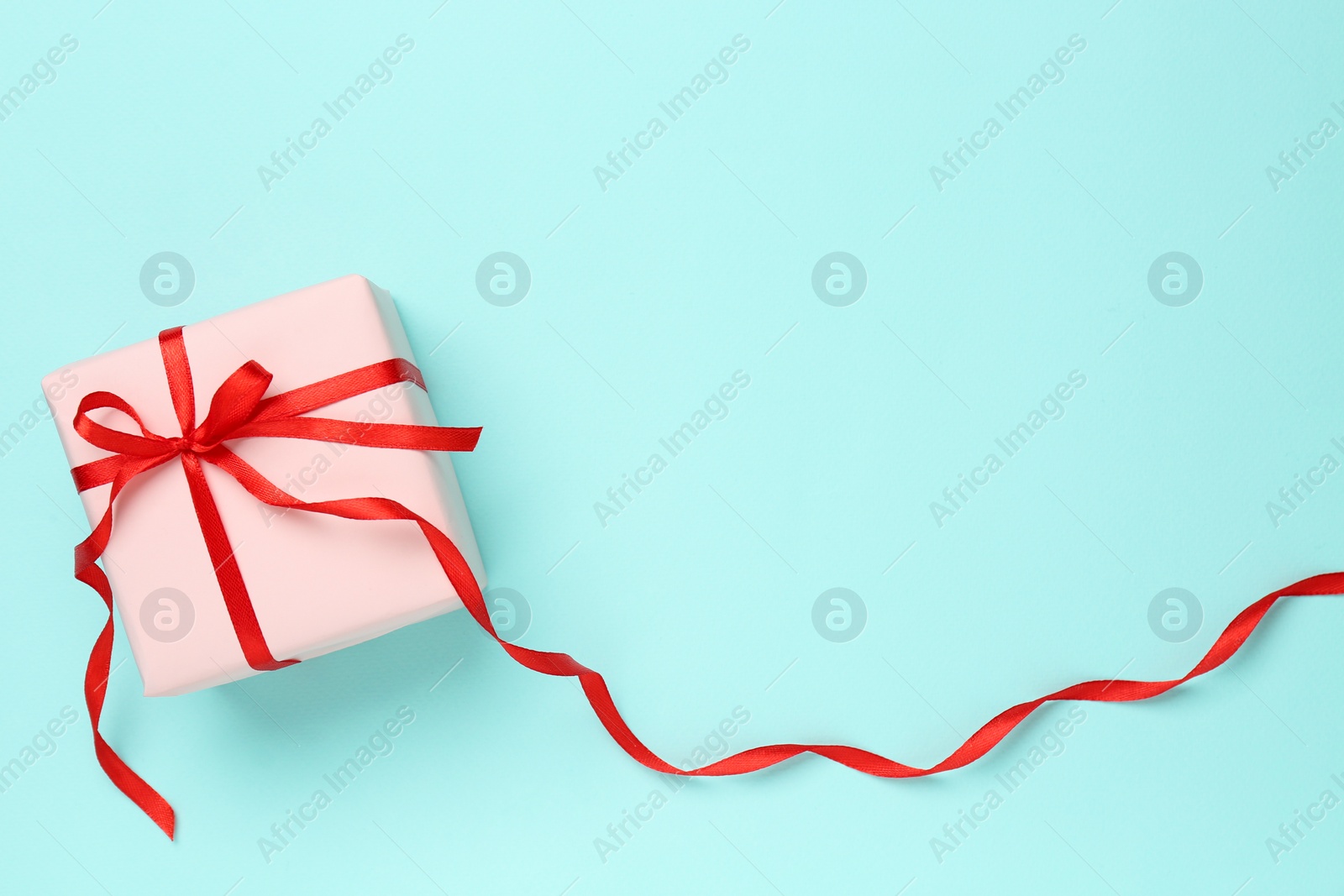 Photo of Gift box with red bow on turquoise background, top view. Space for text