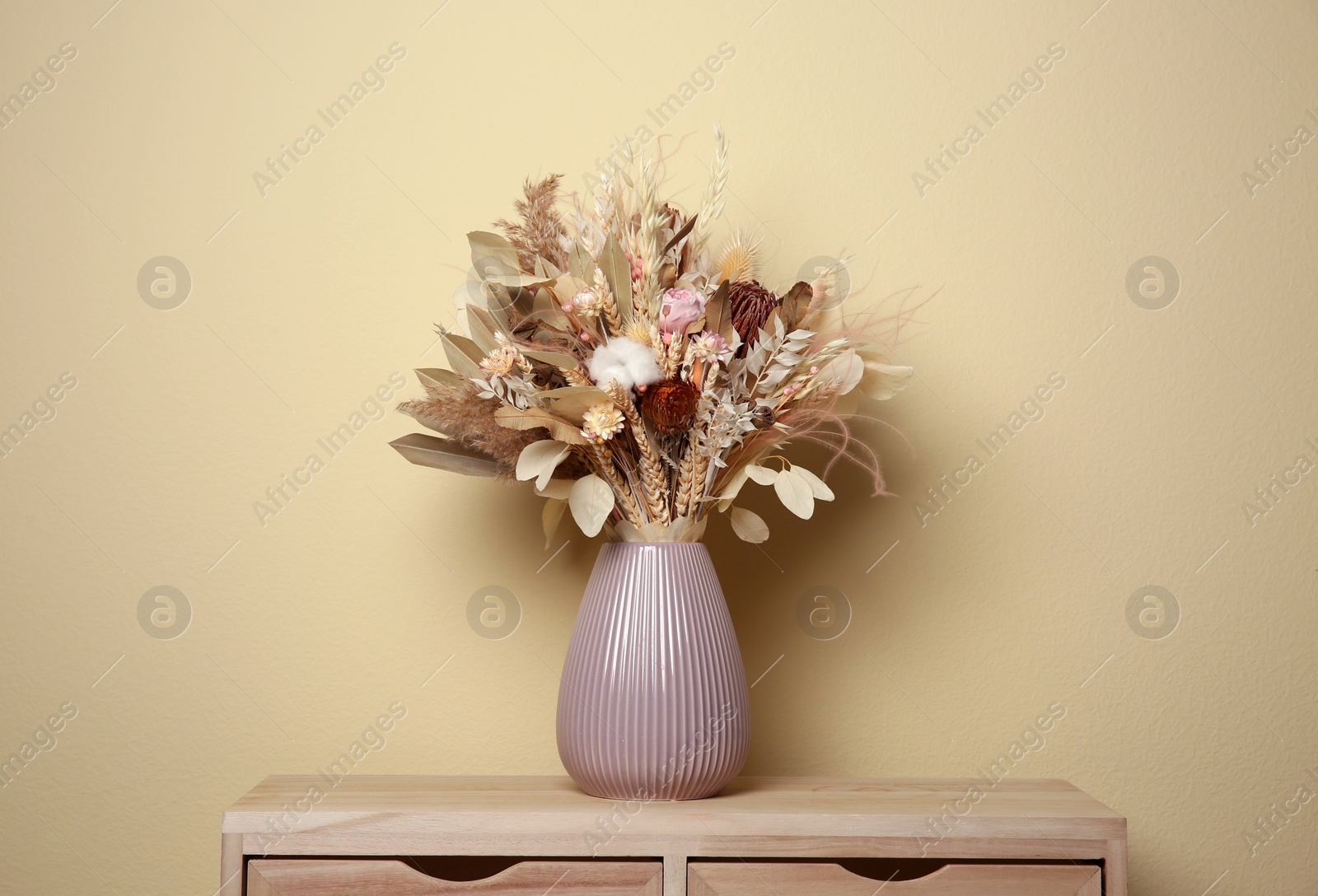 Photo of Beautiful dried flower bouquet in ceramic vase on wooden table near beige wall