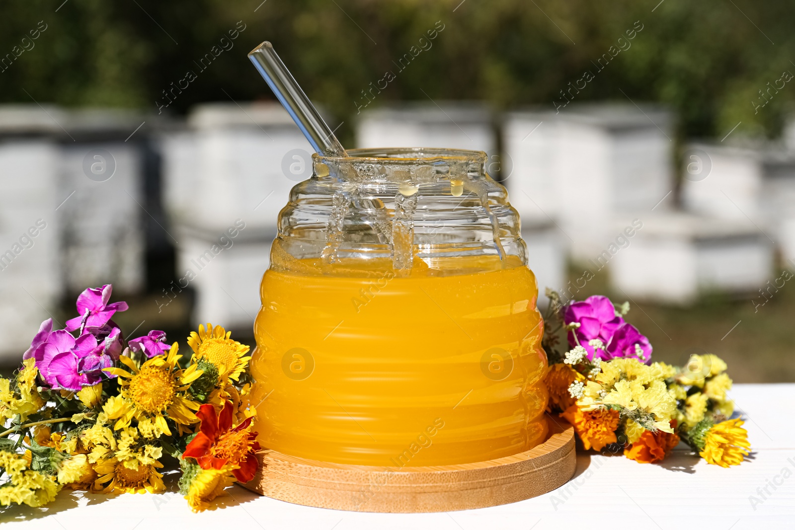 Photo of Delicious fresh honey and beautiful flowers on white wooden table in apiary