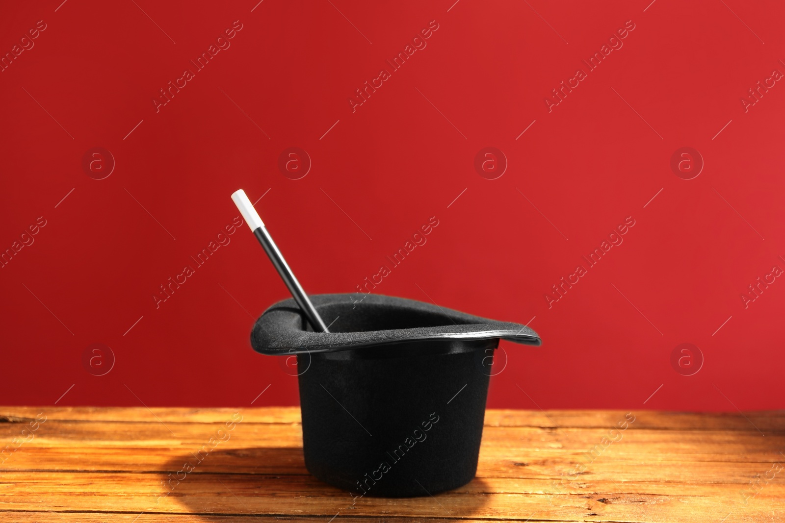 Photo of Magician's hat and wand on wooden table against red background