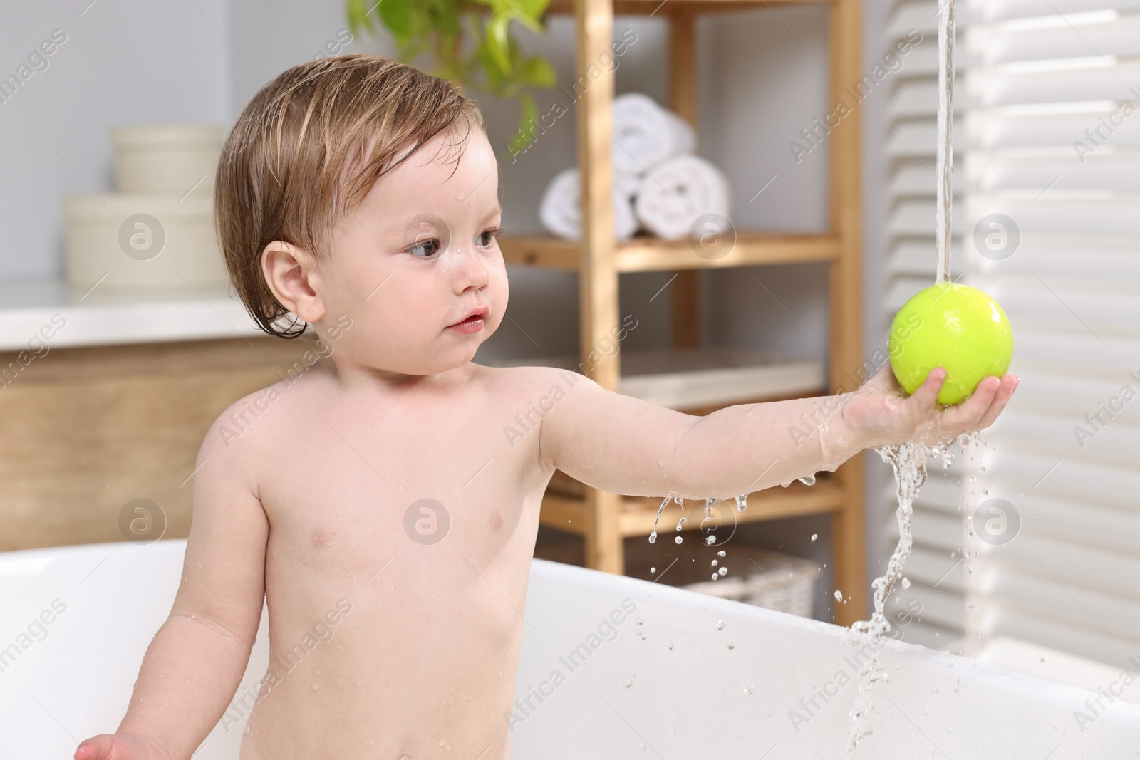 Photo of Cute little child playing with ball in bathtub at home