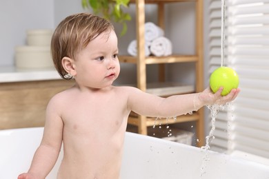 Photo of Cute little child playing with ball in bathtub at home