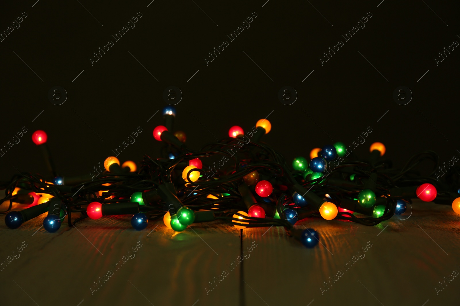 Photo of Beautiful glowing Christmas lights on wooden table against black background