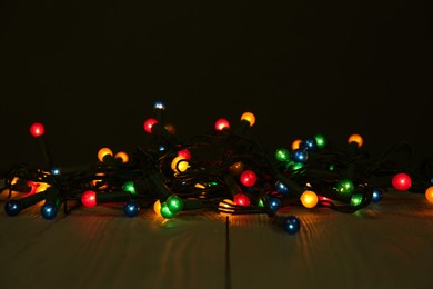 Photo of Beautiful glowing Christmas lights on wooden table against black background