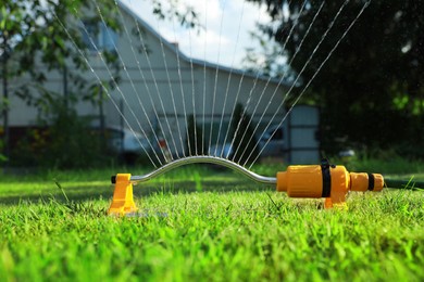 Photo of Automatic sprinkler watering green grass on lawn in garden. Irrigation system