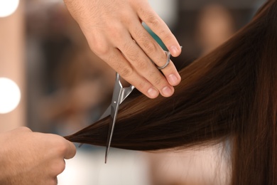 Barber making stylish haircut with professional scissors in beauty salon, closeup