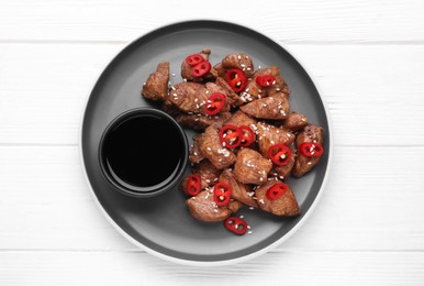 Plate with tasty soy sauce and roasted meat on white wooden table, top view