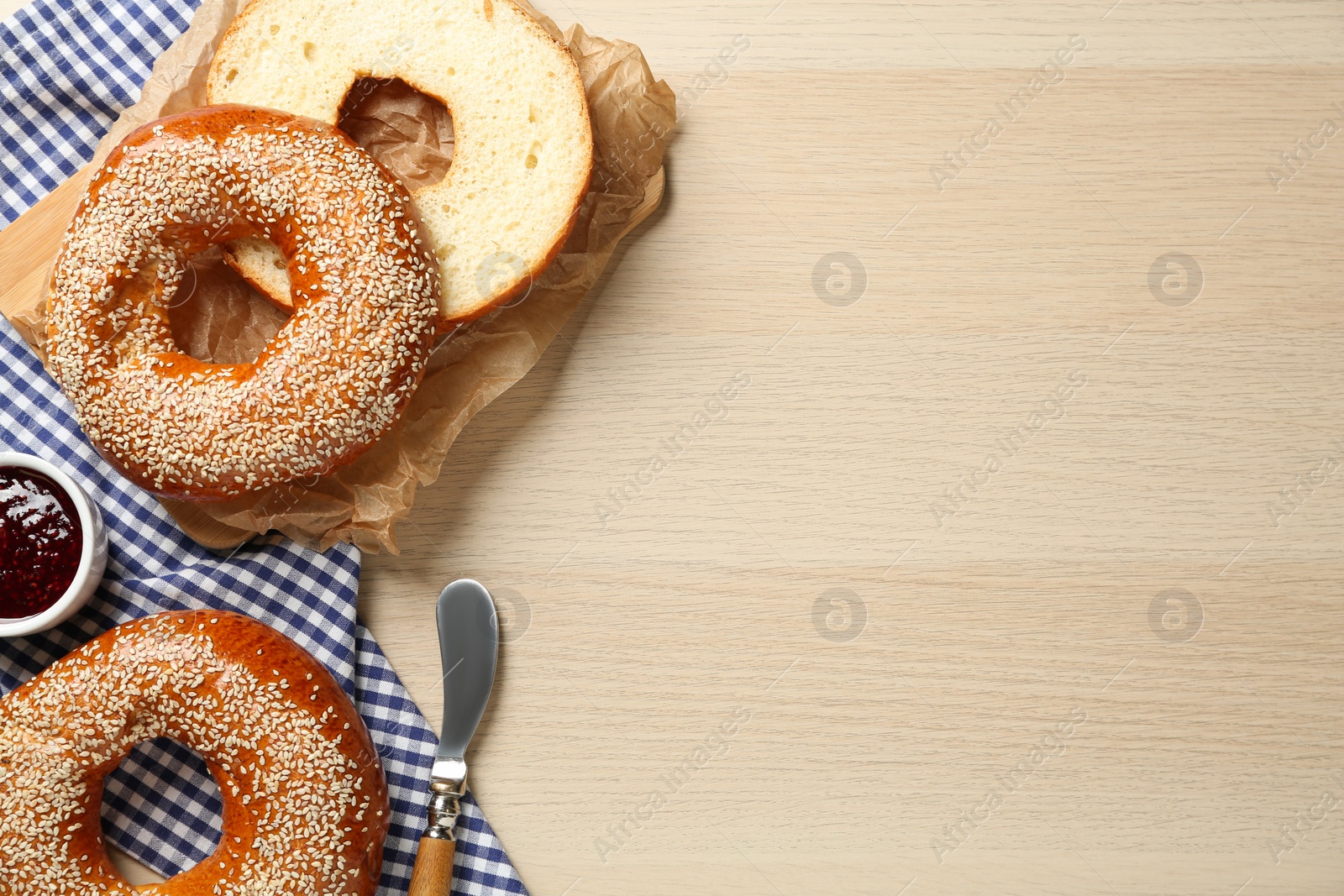 Photo of Delicious fresh bagels with sesame seeds and jam on wooden table, flat lay. Space for text