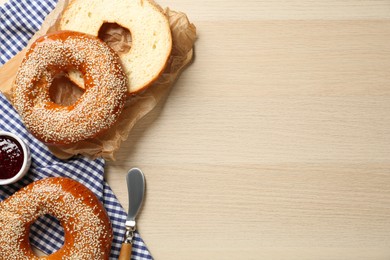 Delicious fresh bagels with sesame seeds and jam on wooden table, flat lay. Space for text