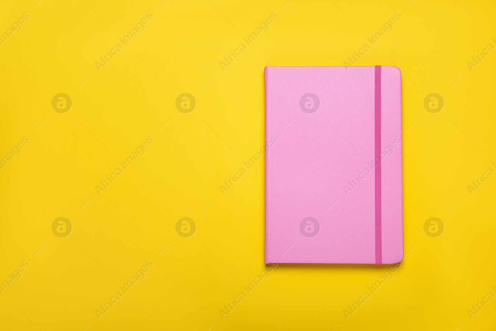 Photo of Closed pink notebook on yellow background, top view. Space for text