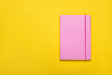 Photo of Closed pink notebook on yellow background, top view. Space for text