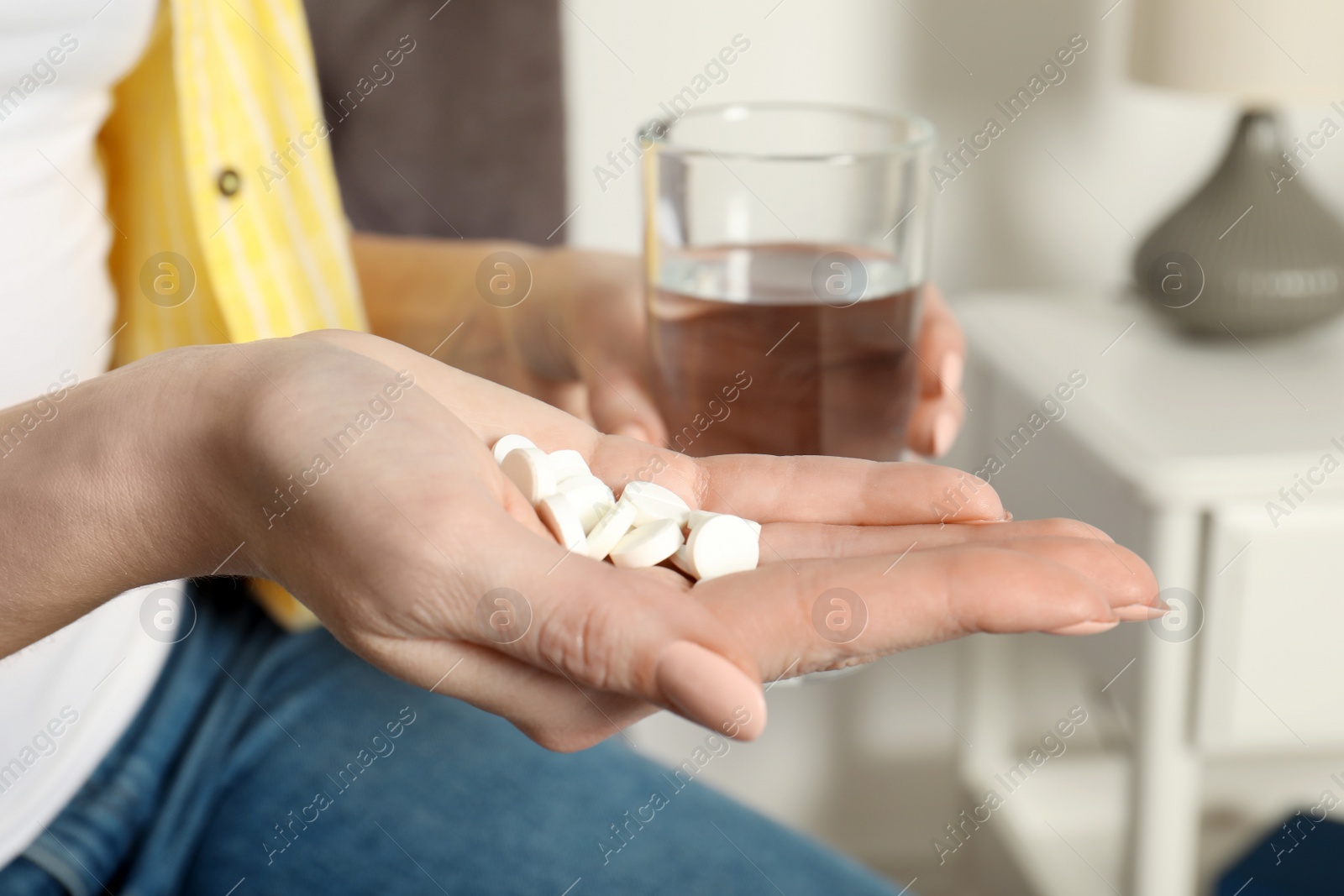 Photo of Woman with pills and glass of water indoors, closeup