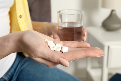 Woman with pills and glass of water indoors, closeup