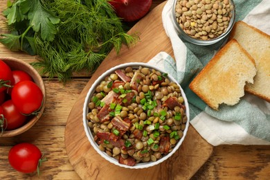 Photo of Delicious lentils with bacon and green onion in bowl served on wooden table, flat lay