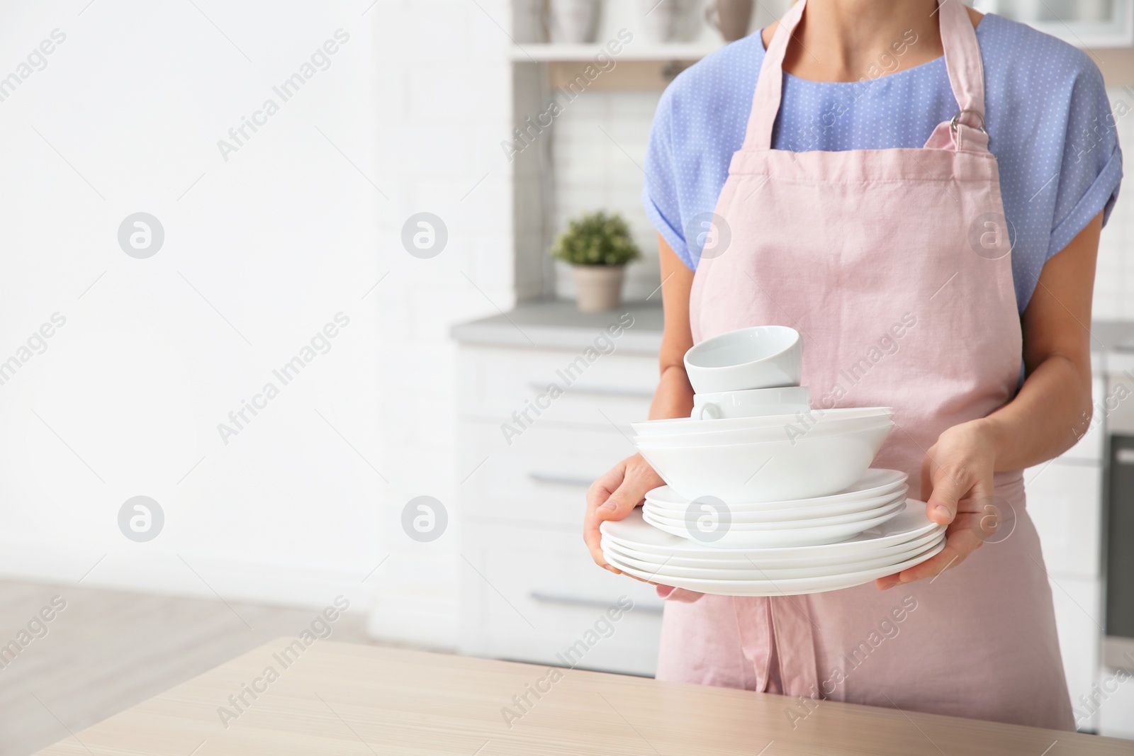 Photo of Woman with clean dishes and cups in kitchen, closeup. Space for text