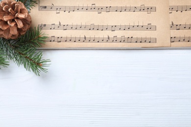 Photo of Christmas music sheets and fir tree branch and space for text on white wooden background, top view