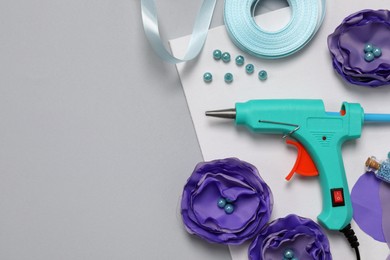 Photo of Hot glue gun, textile flowers and handicraft materials on grey background, flat lay. Space for text