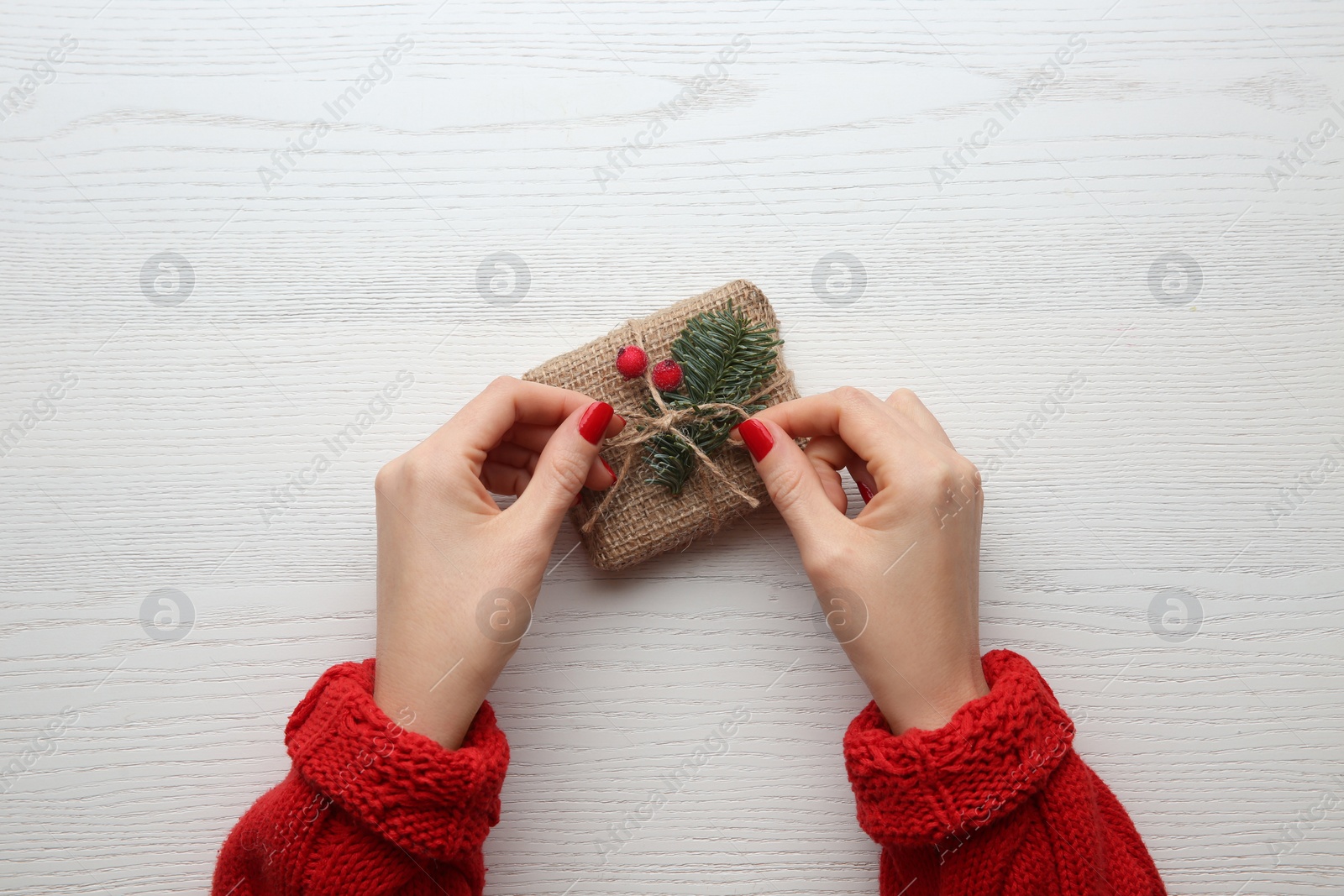 Photo of Woman holding Christmas gift box at white wooden table, top view