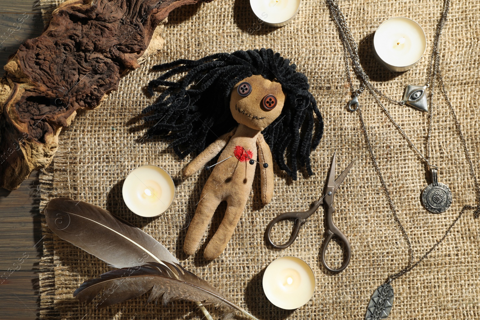 Photo of Voodoo doll with pins surrounded by ceremonial items on wooden table, flat lay