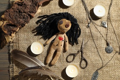 Voodoo doll with pins surrounded by ceremonial items on wooden table, flat lay
