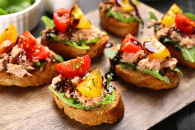 Photo of Delicious bruschettas with balsamic vinegar, tomatoes, arugula and tuna on table, closeup