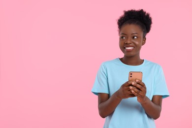 Photo of Happy young woman with smartphone on pink background. Space for text