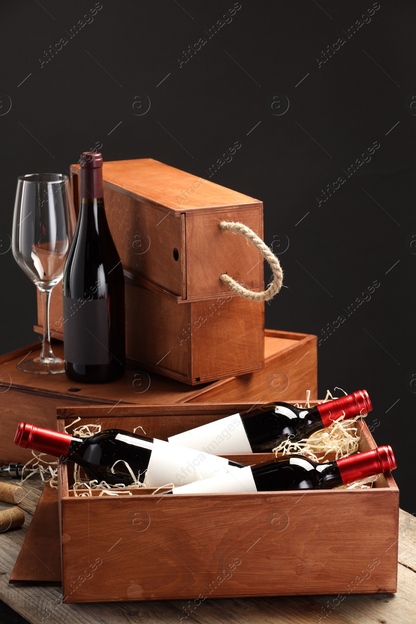 Photo of Boxes with wine bottles and glass on wooden table against black background