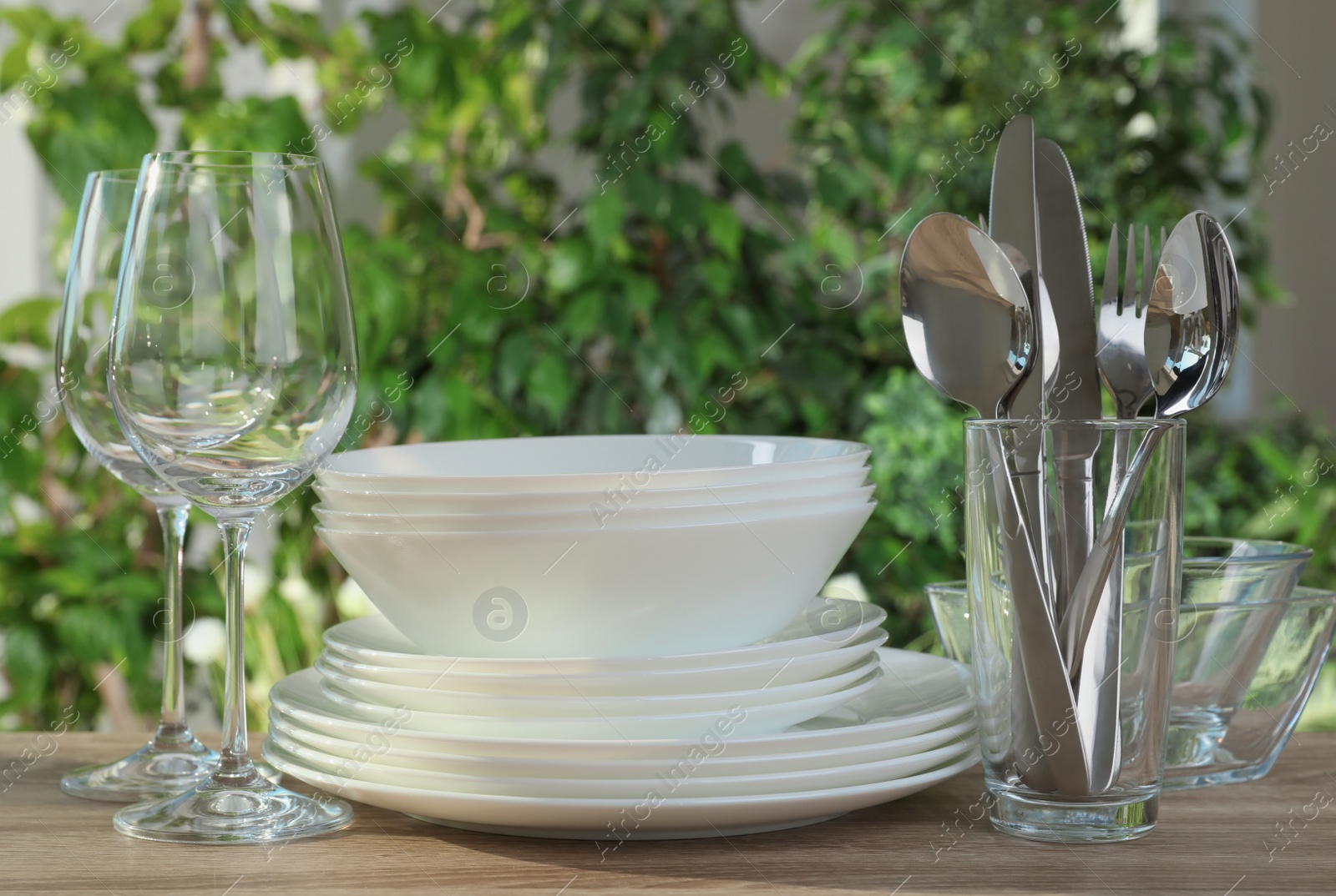 Photo of Clean dishes, shiny cutlery and glasses on wooden table against blurred background