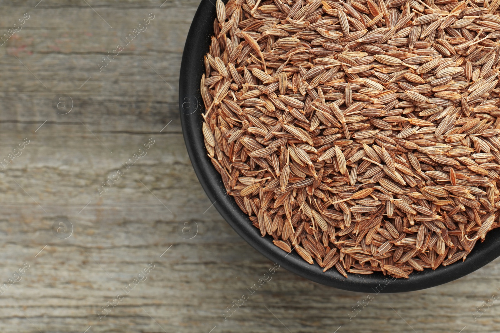 Photo of Bowl of caraway seeds on wooden table, top view. Space for text