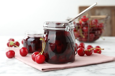Photo of Jars of pickled cherries and fresh fruits on white marble table