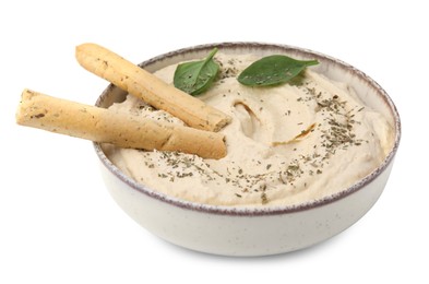 Photo of Bowl of delicious hummus with grissini sticks, basil leaves and spices isolated on white