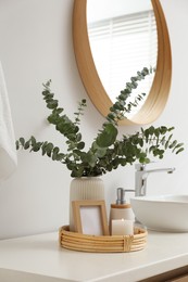 Photo of Vase with eucalyptus branches and toiletries near vessel sink in bathroom. Interior design