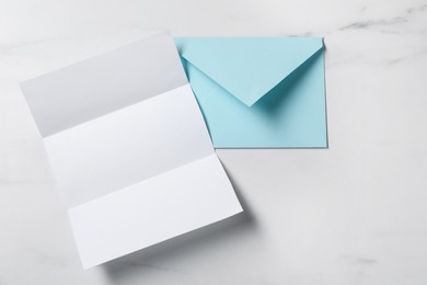 Photo of Blank sheet of paper and letter envelope on white marble table, top view