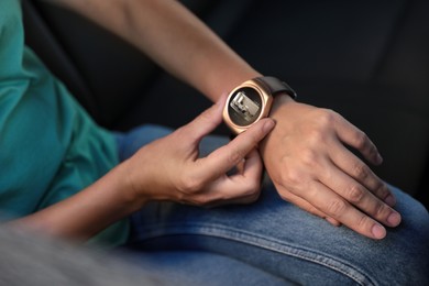 Woman checking home security system via smartwatch app in car, closeup. Image of room through CCTV camera on display